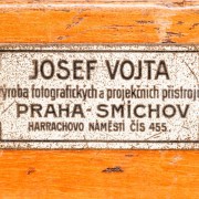 Neobvyklý tvar továrního štítku. Zajímavé je i znění předmětu podnikání. Štítek pochází z doby, kdy Josef Vojta vyráběl kromě fotokomor i velké projekční přístroje, zvané laterna magica.